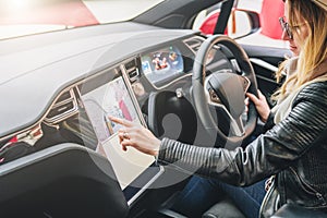 Woman sits behind wheel in car and uses electronic dashboard. Girl traveler looking for way through navigation system.