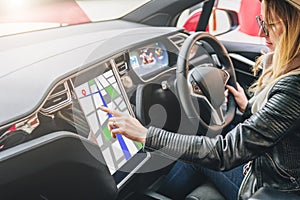 Woman sits behind wheel in car and uses electronic dashboard. Girl traveler looking for way through navigation system.