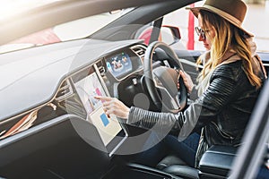 Woman sits behind wheel in car and uses electronic dashboard. Girl traveler looking for way through navigation system.