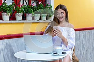 Woman sits in a brasserie and works on laptop and smartphone