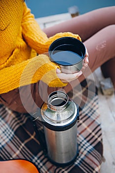 Woman sits on a bridge on a lake with an autumn landscape and drinks hot tea