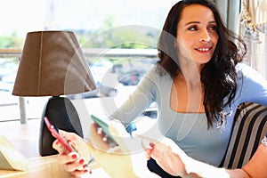 Woman sits in cafe with friend and holds smartphones in her hand