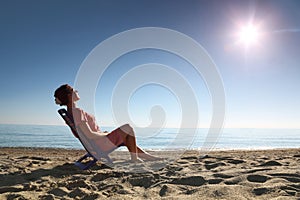 Woman sits on chair on sea-shore by person to sun