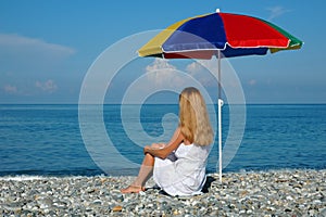 Woman sits at coast under umbrella