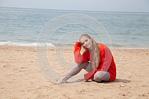 A woman sits at a deserted sandy beach looking at sea
