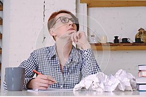 Woman sits at a desk in front of a blank sheet of paper with a red pencil