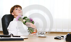 Woman sits at the desk hugging flowers bouquet