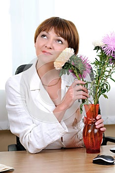 Woman sits at the desk hugging flowers bouquet