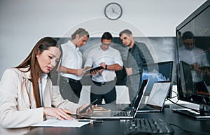 Woman sits in front of laptop and displays. Team of stockbrokers works in modern office with many display screens