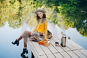 Woman sits with a guitar on a bridge on a lake with an autumn landscape