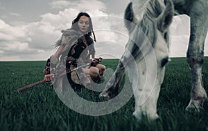 Woman sits on meadow in image of warrior amazon near grazing horse