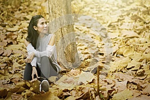 Woman sits at park with dried autumn foliage