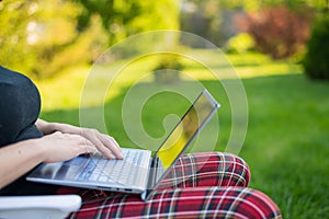 Woman sits in a park and types on the computer while shopping online. The girl maintains a social distance and works