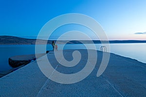 A woman sits on a pier on a bench and looks at the sunset