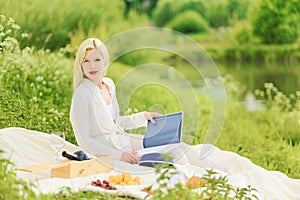 A woman sits on a plaid with a book in her hands. Glamorous Blonde on a picnic alone