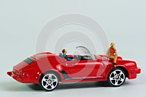 A woman sits on a red cabriolet sports car with driver