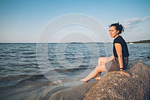 Woman sits on the rock and lookin for lake view