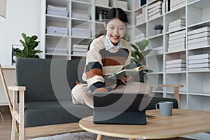 A woman sits on a sofa, using her notebook and tablet computer simultaneously to study online, efficiently managing her photo