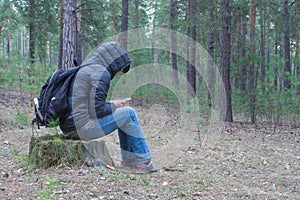 A woman sits on a stump in the woods early in the morning and ch