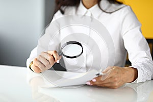 Woman sits at table and holds magnifying glass and documents in her hands.