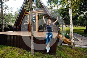 Woman sits on terrace of log cabin in the morning and stretching arms