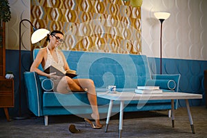 Woman sits on a vintage blue sofa in a old-fashioned living room and reading the book