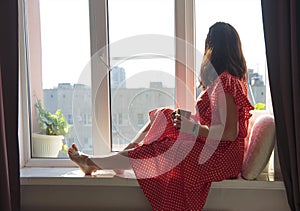 A woman sits on a window seat in the summer sun and looks out at the street