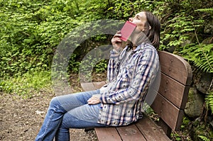 Woman sits on a wooden bench in a forest park by the path and lo