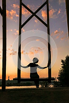 A woman sits on a wooden swing against the backdrop of sunset in Kyiv