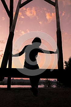 A woman sits on a wooden swing against the backdrop of sunset in Kyiv