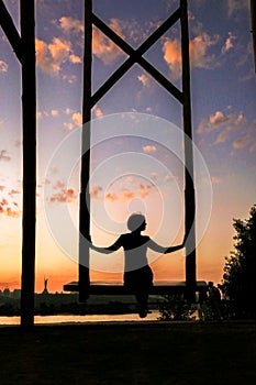 A woman sits on a wooden swing against the backdrop of sunset in Kyiv