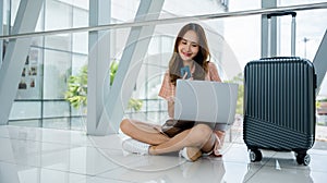 woman sitting on the airport floor, typing on her phone and laptop