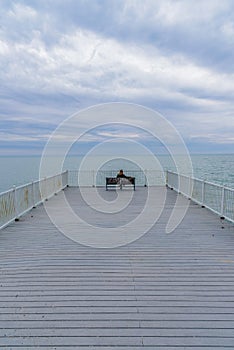 Woman sitting alone on bench at end of pier