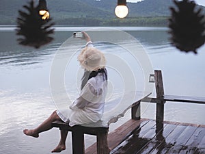 woman sitting alone on the bench taking photograph at sunrise beach background