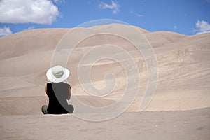 Woman sitting alone in desert sand dunes.