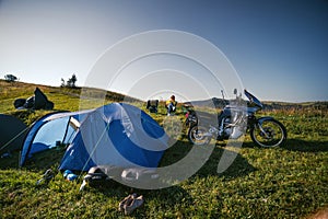 The woman is sitting alone on the folding chair. Top of the mountain a with touring motorcycle. camping equipment, off road jorney photo