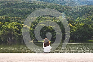 A woman sitting alone by the lake looking at the mountains with cloudy and green nature