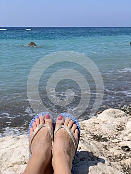 A woman sitting alone on stone near the sea with her feet pointing down