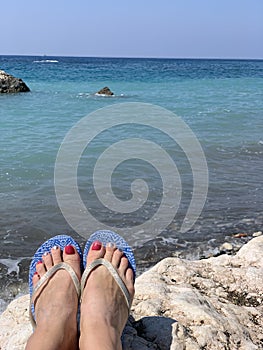 A woman sitting alone on stone near the sea with her feet pointing down