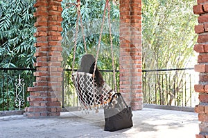 A woman sitting alone on a swing amidst of pillars made up of bricks at sunrise