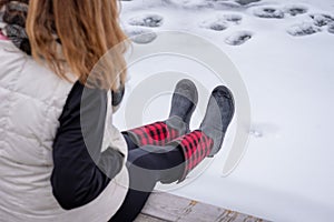 Woman sitting on edge of pier in winter with red plaid boots