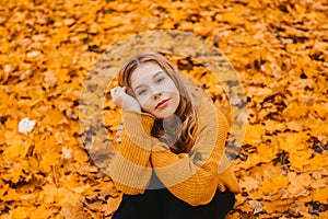 A woman is sitting in an autumn park. Girl teenager on a background of autumn leaves. Fashion photo
