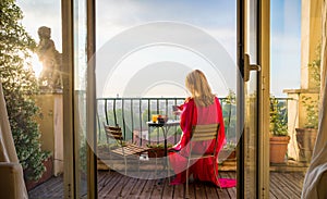 Woman sitting on balcony and overlooking city in morning at sunrise