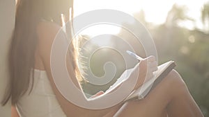 Woman sitting at balcony and writing in diary with garden on the background