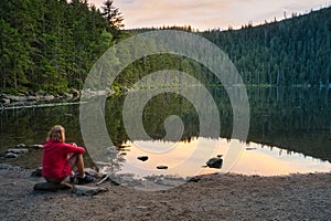 A woman sitting on the bank of beautiful Devil`s Lake in the Bohemian Forest, Czech Republic