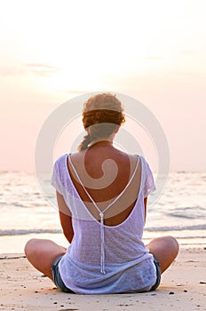 Woman is sitting on beach at sunrise