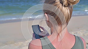 Woman sitting on beach and texting on smart phone