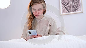 Woman sitting at bed at home, having breakfast and using smartphone