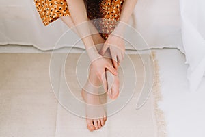 Woman sitting on the bed massages her foot, close-up.