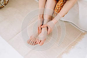 Woman sitting on the bed massages her foot, close-up